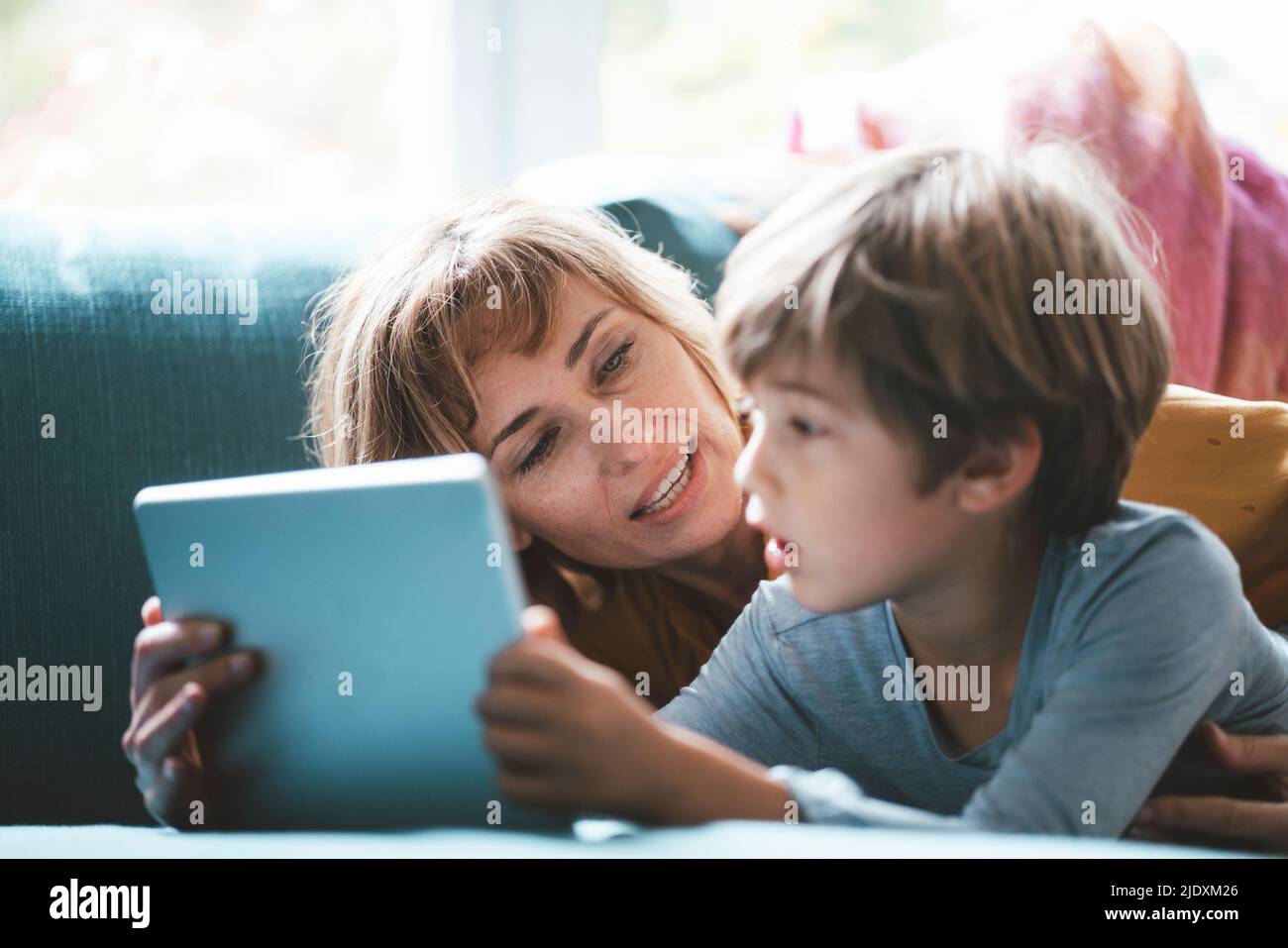 Reife Frau mit Junge mit Tablet-PC, der zu Hause auf dem Sofa liegt Stockfoto