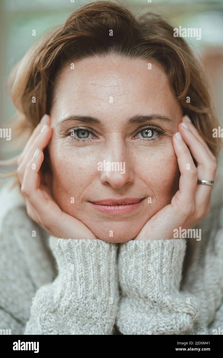 Lächelnde blonde Frau mit Kopf in den Händen Stockfoto