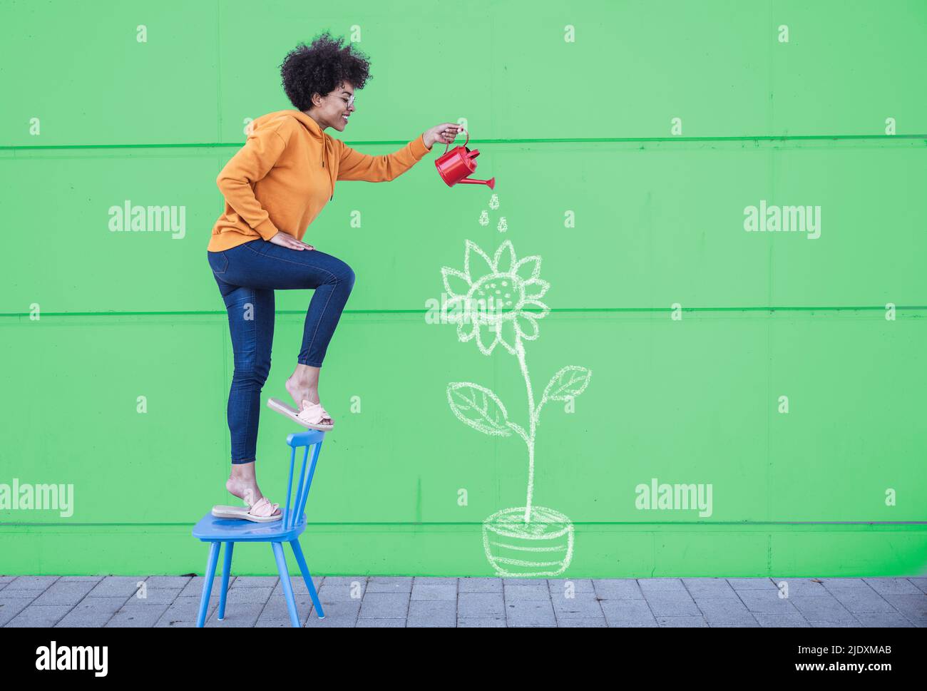 Frau, die auf einem Stuhl steht und Blumen an der Wand bewässert Stockfoto