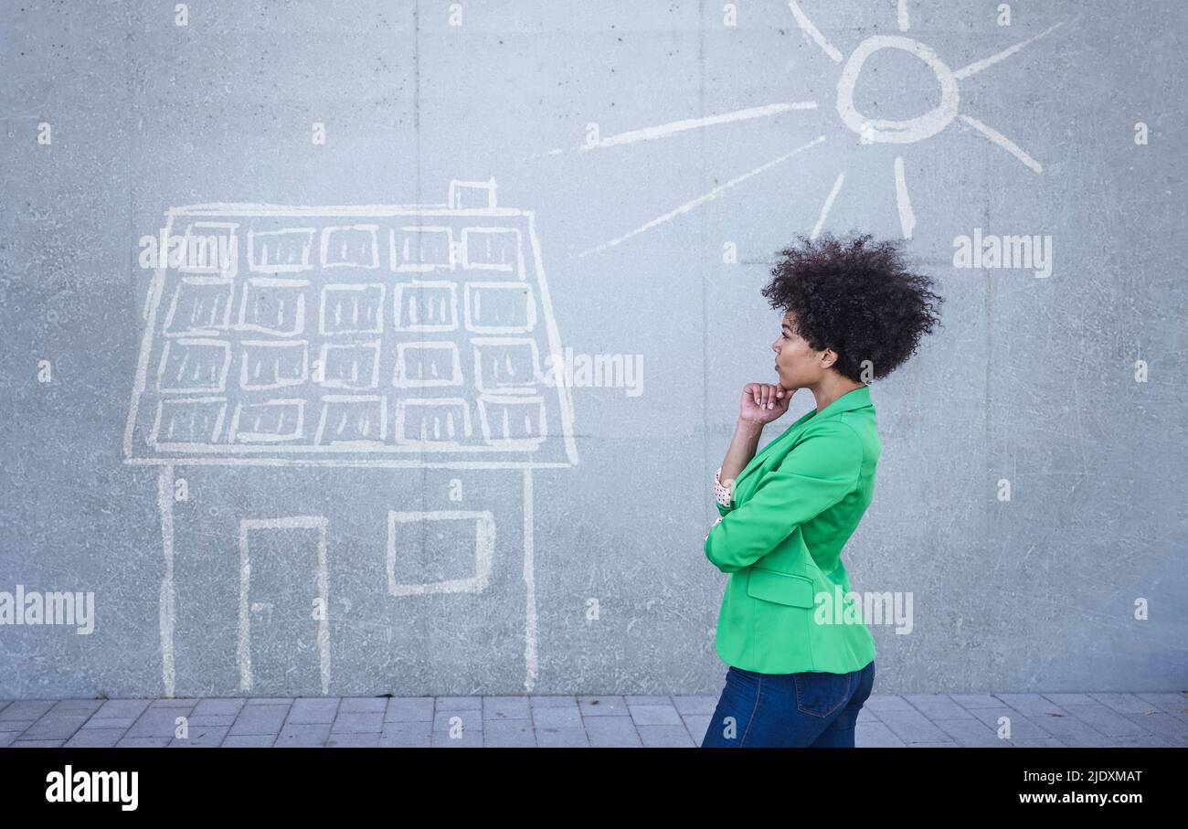 Junge Frau, die ein bemaltes Haus mit Sonnenkollektoren an der Wand ansieht Stockfoto
