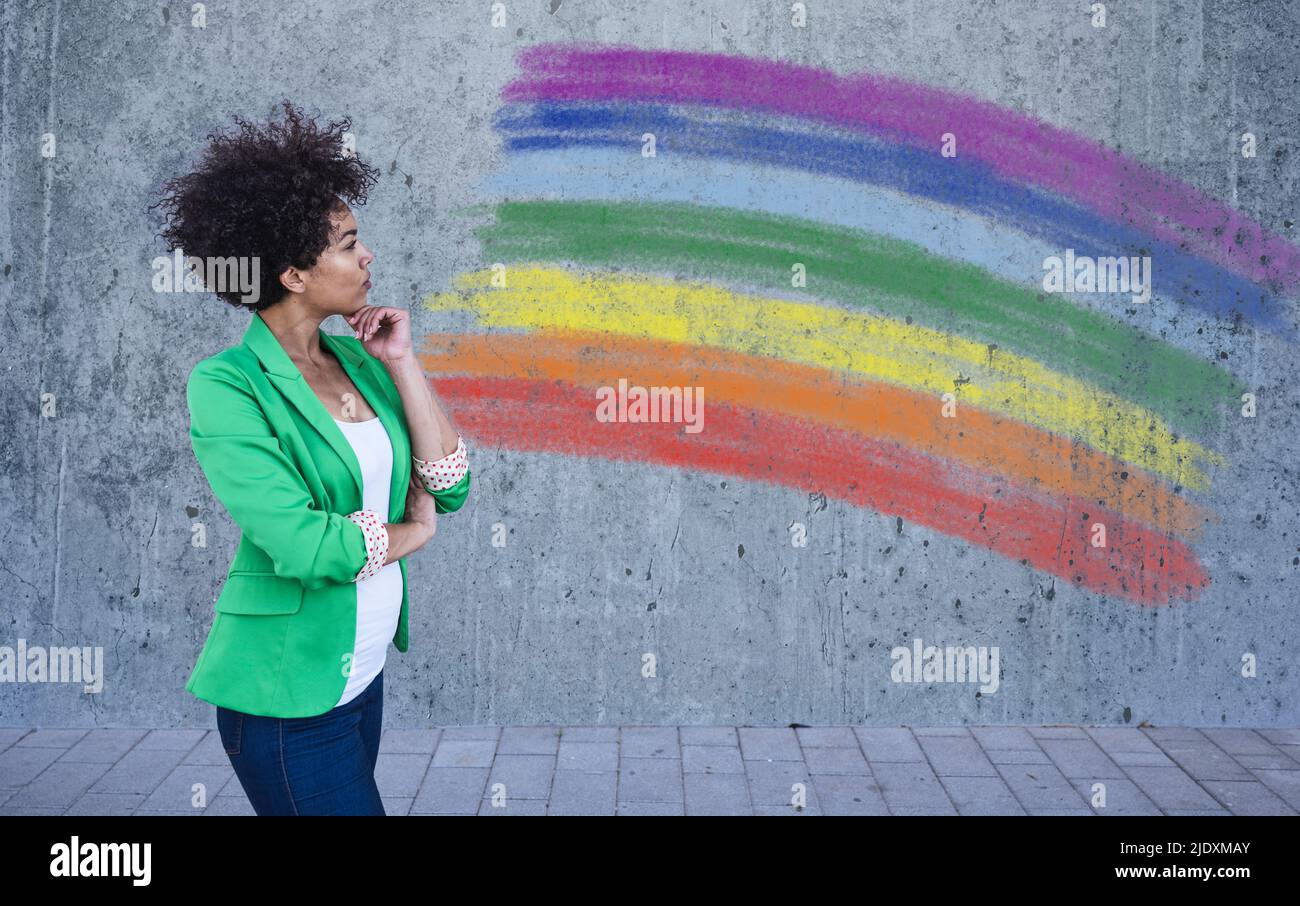 Junge Frau, die auf die gemalte Regenbogenfahne an der Wand schaut Stockfoto