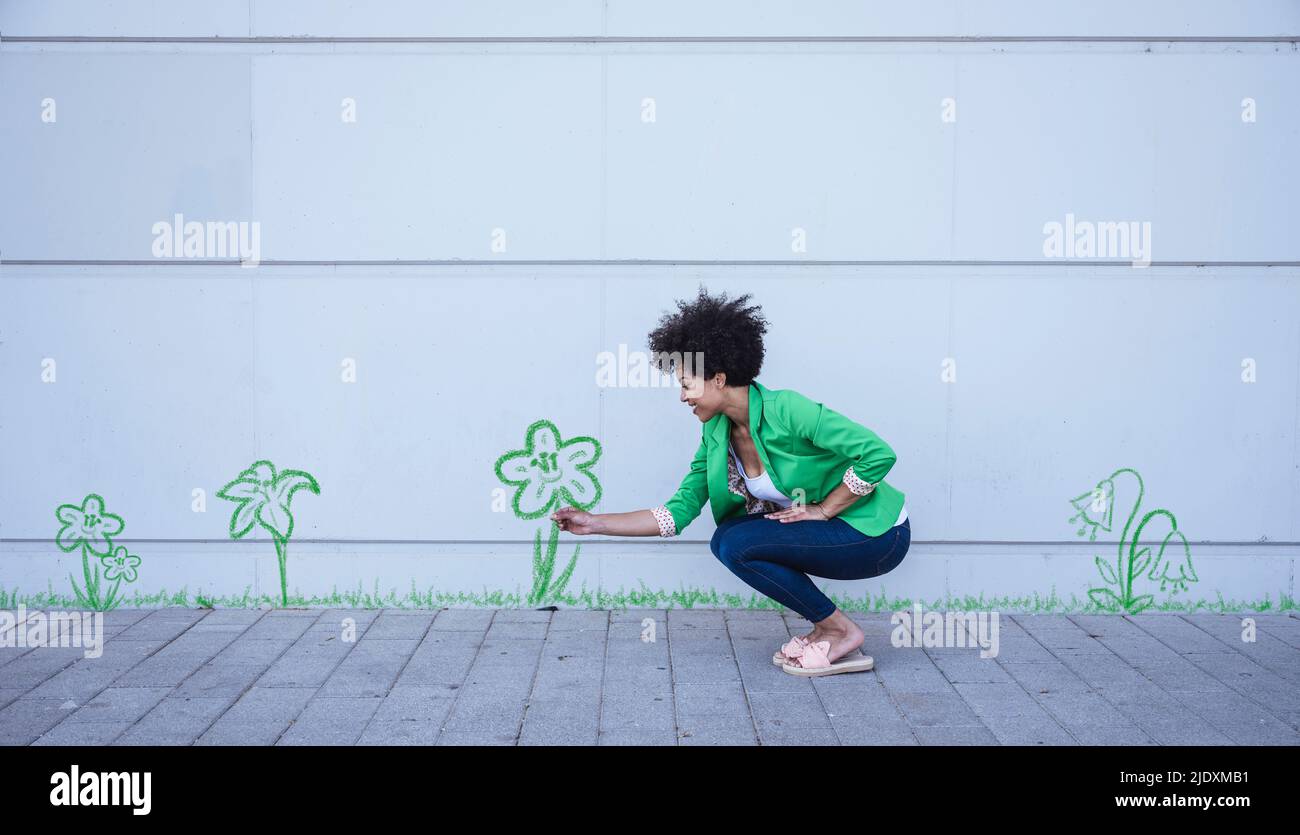 Hockende Frau, die die gemalte Blume von der Wand zupfte Stockfoto