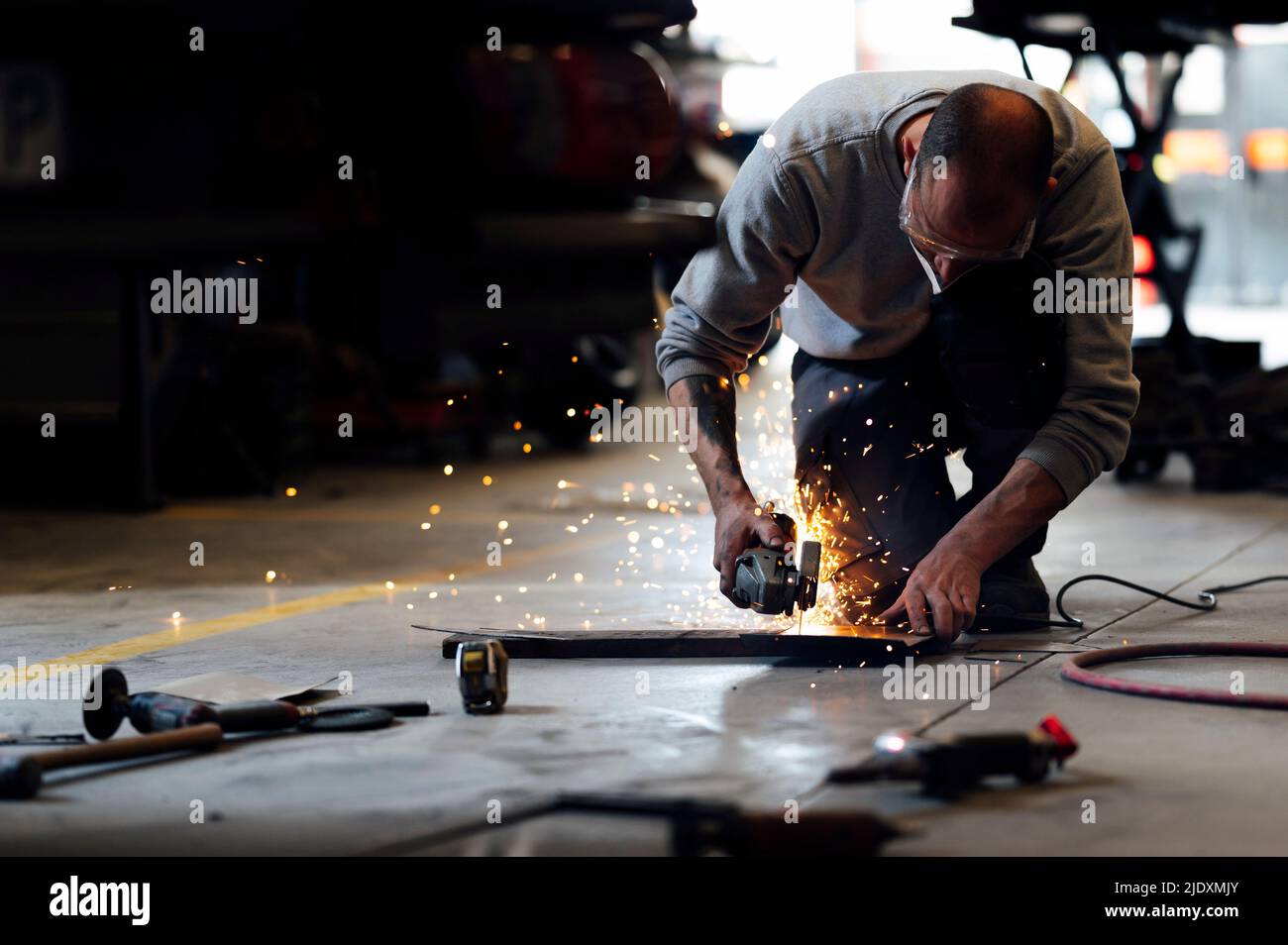 Mechaniker, der Metall auf dem Boden in der Garage schneidet Stockfoto