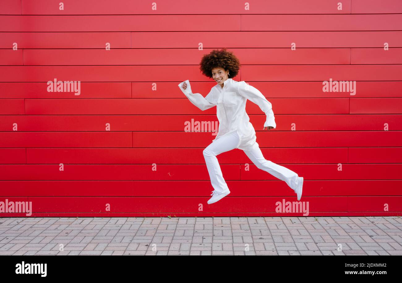 Afro-Frau springt an der roten Wand Stockfoto