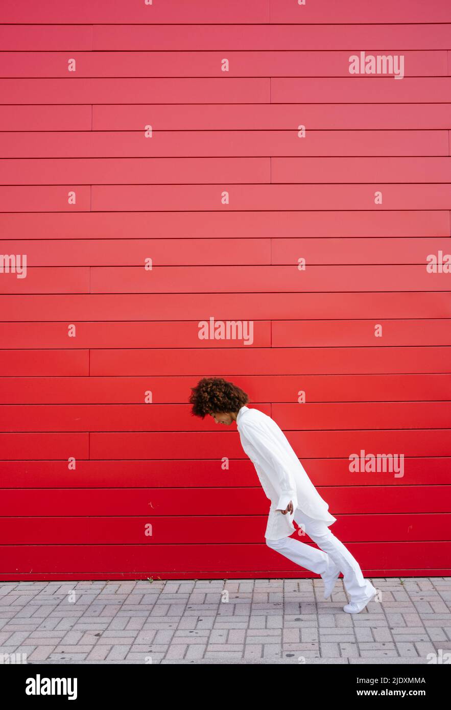 Junge Frau, die sich an der roten Wand nach vorne auf dem Fußweg lehnt Stockfoto