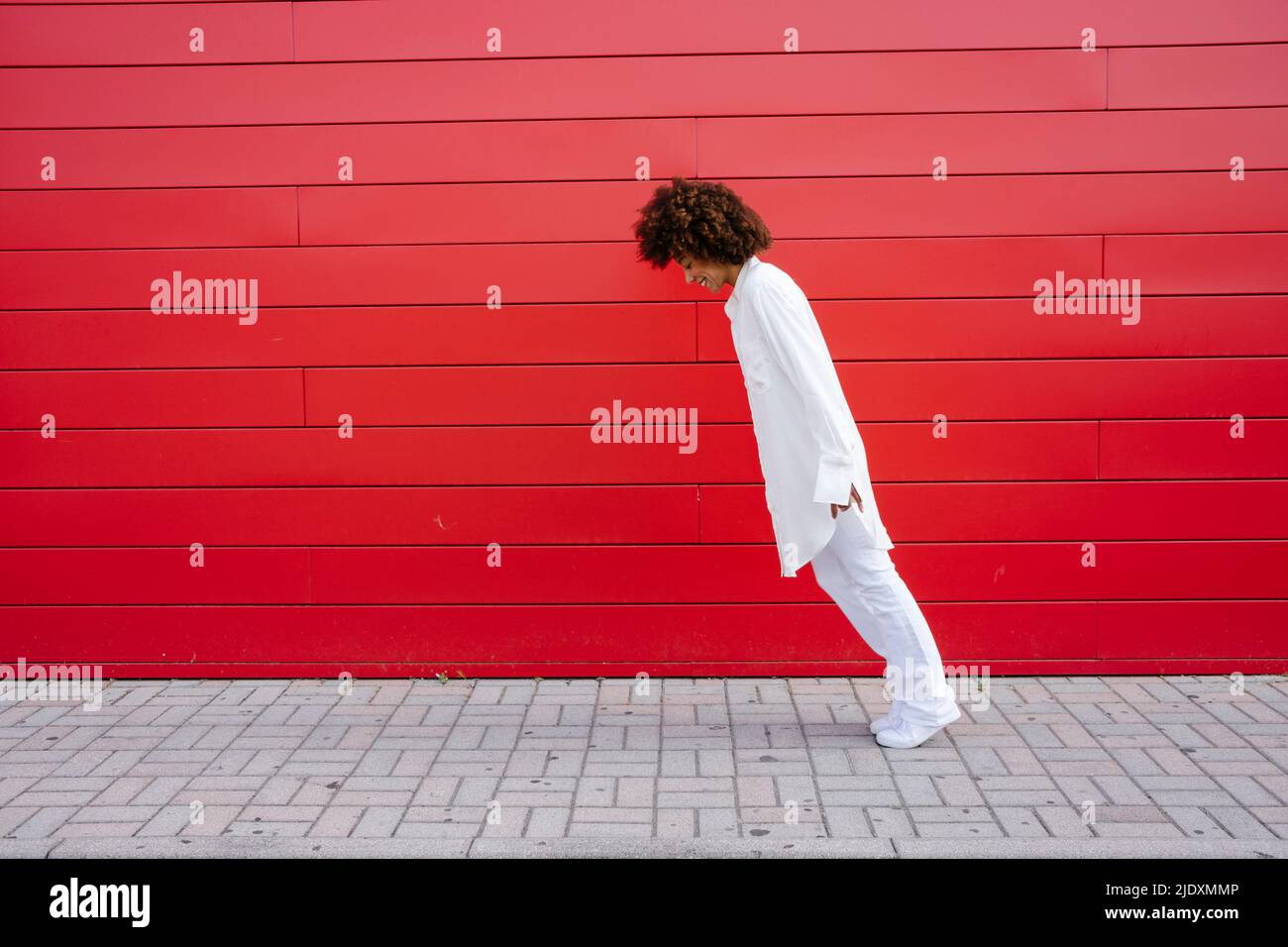Junge Frau, die sich an der roten Wand nach vorne lehnt Stockfoto