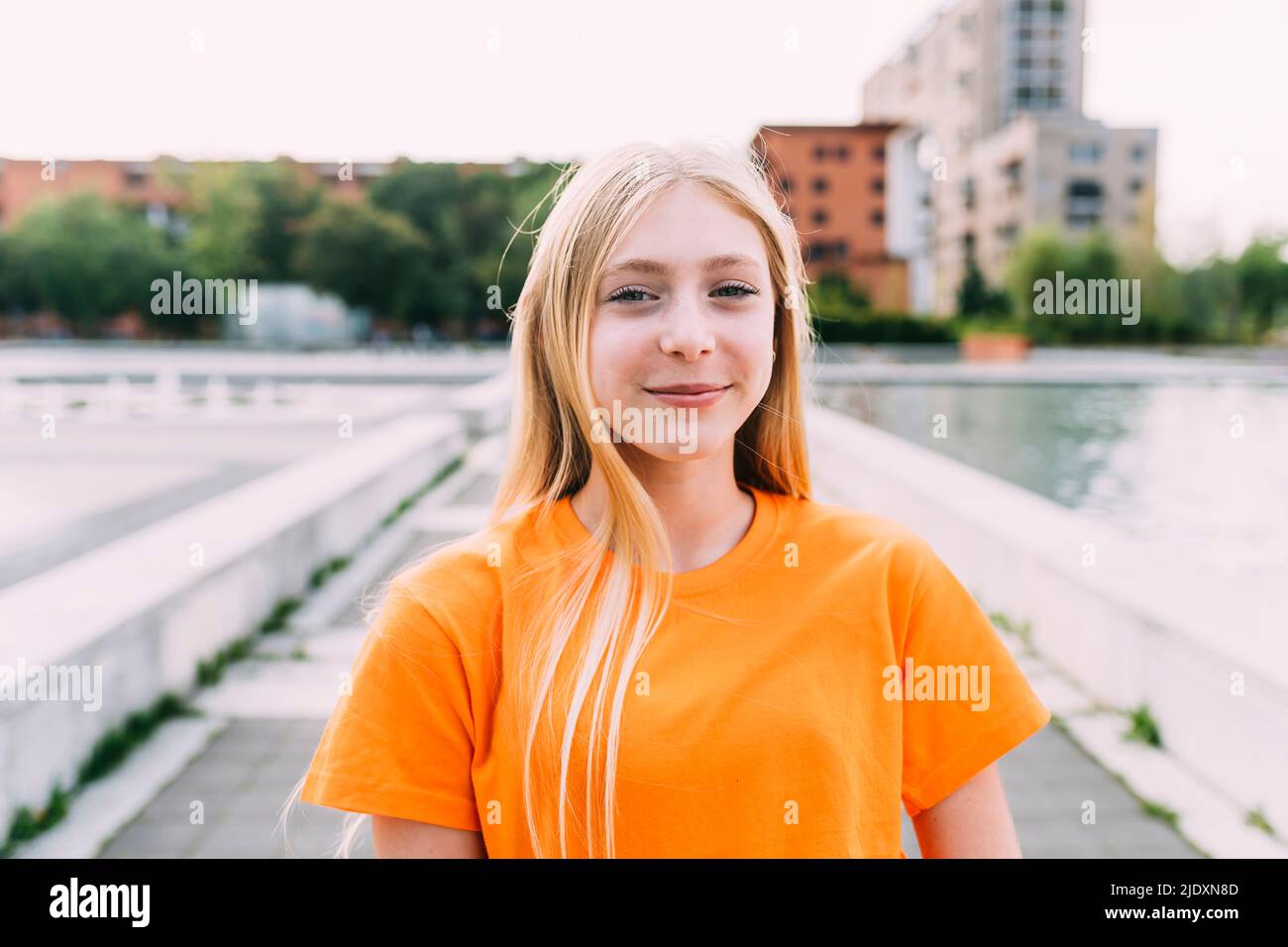 Fröhliches Mädchen mit blonden Haaren in orangefarbenem T-Shirt Stockfoto