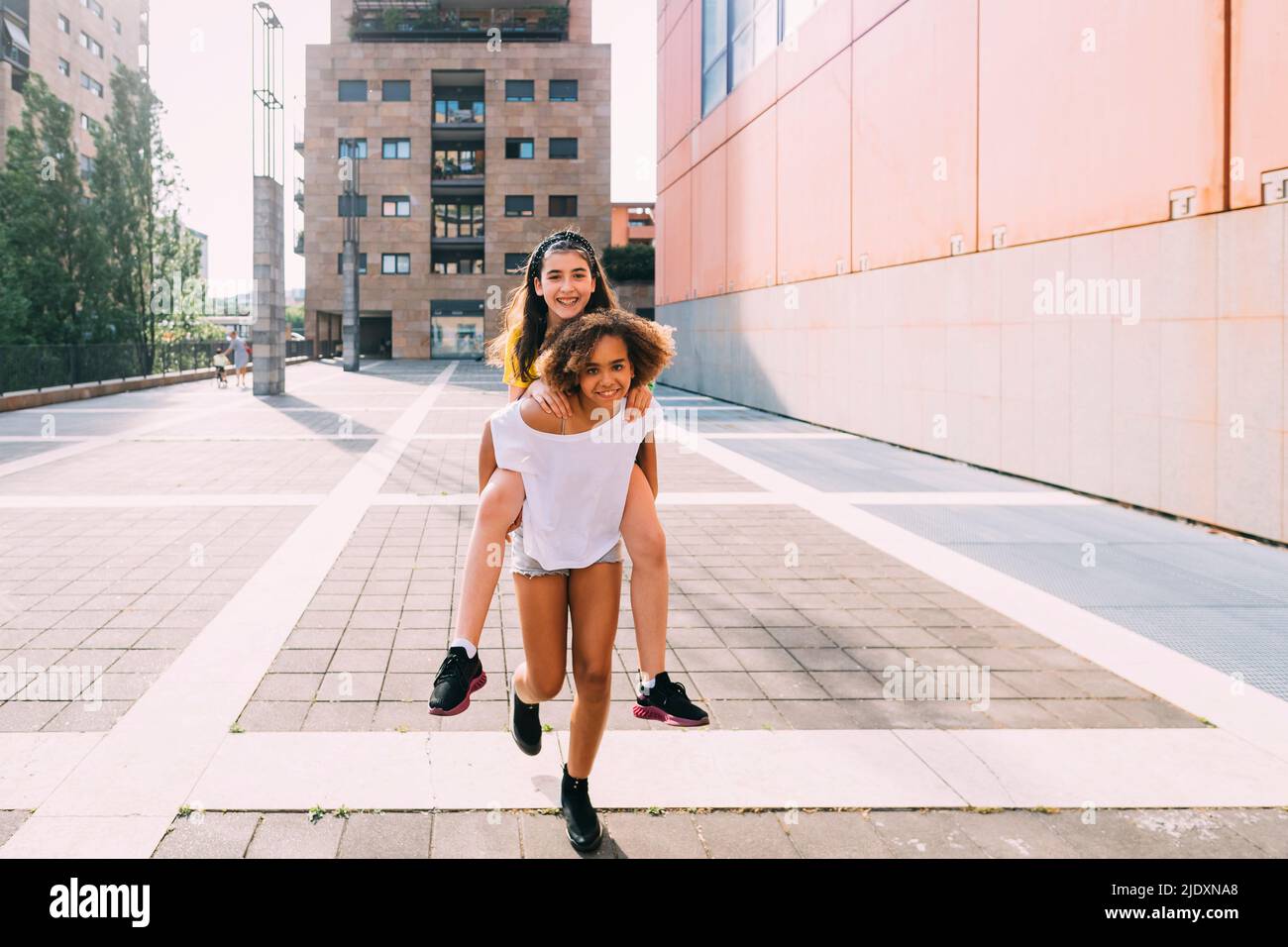 Lächelndes Mädchen gibt Huckepack Fahrt zu Freund an sonnigen Tag Stockfoto