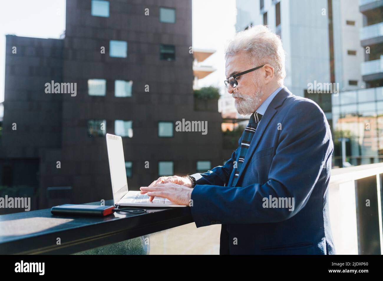 Leitender Geschäftsmann, der einen Laptop mit Solarladegerät auf dem Bürobalkon verwendet Stockfoto