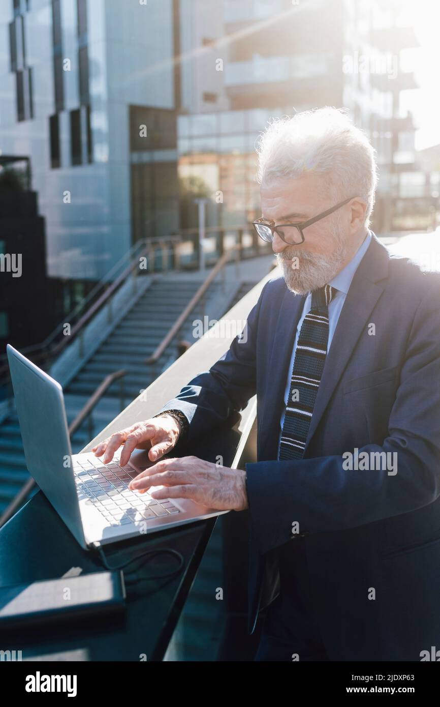 Leitender Geschäftsmann, der an einem Laptop mit Solarladegerät außerhalb des Bürogebäudes arbeitet Stockfoto