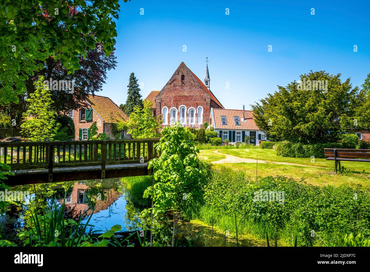 Deutschland, Niedersachsen, Krummhorn, kleine Brücke über stehendes Wasser mit Loquard-Kirche im Hintergrund Stockfoto