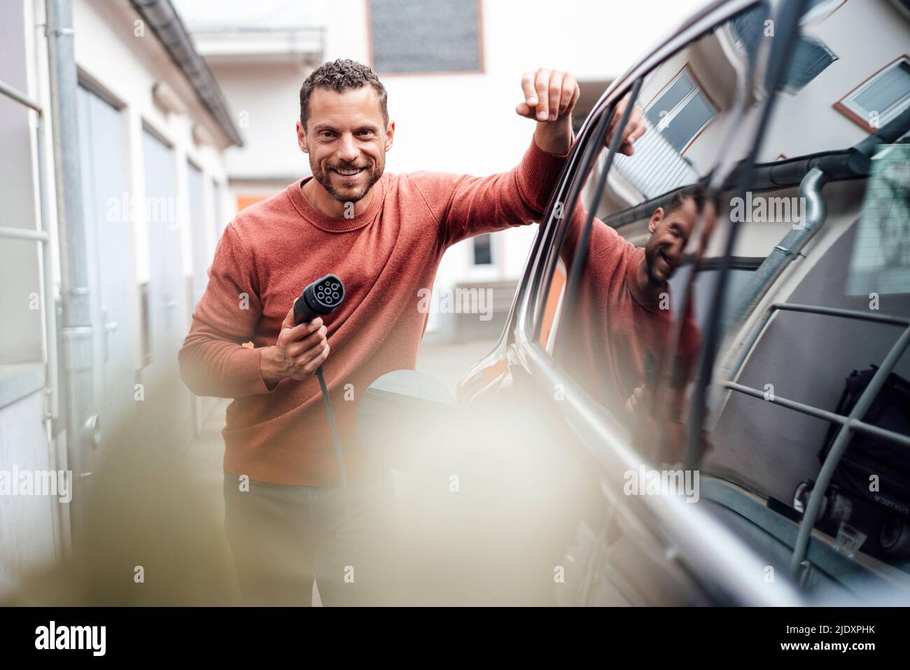 Lächelnder Mann, der das Ladekabel an einem Elektroauto hält Stockfoto