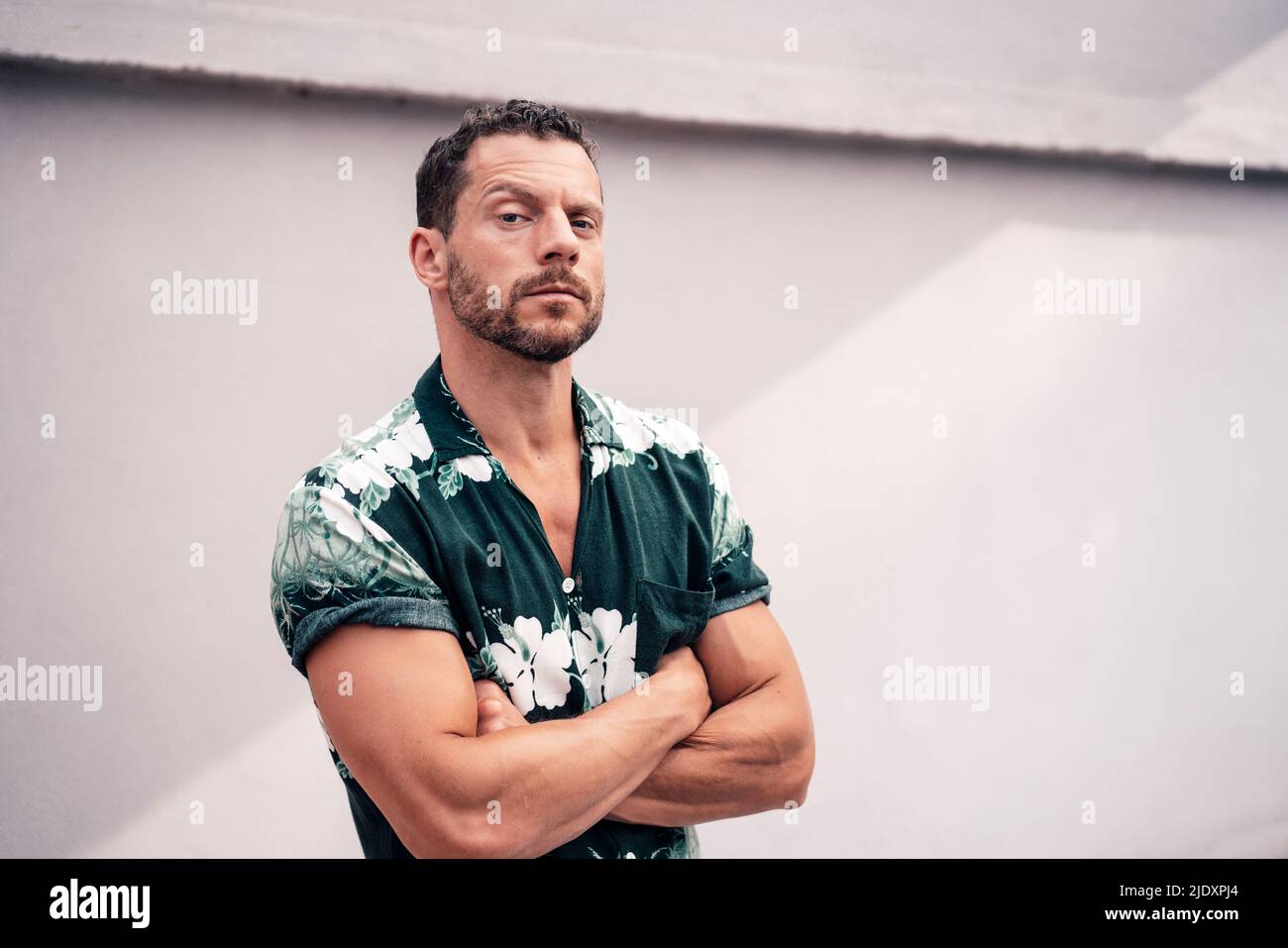 Reifer Mann mit gekreuzten Armen, die die Augenbraue anheben und vor der Wand stehen Stockfoto