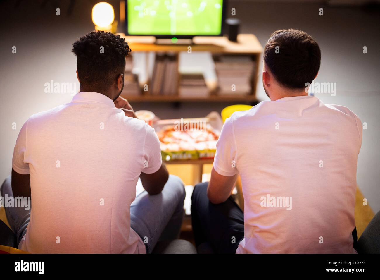 Junge Mitbewohner sehen sich das Fußballspiel zu Hause zusammen an Stockfoto