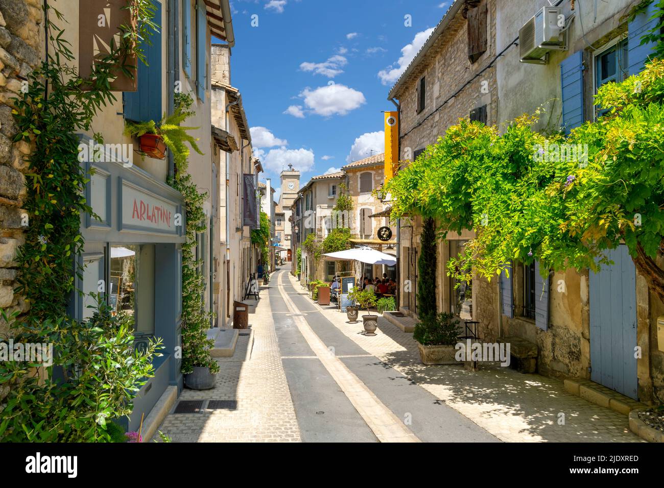 Eine der vielen typischen Straßen und Gassen mit bunten Straßencafés und Geschäften in der historischen Stadt Saint-Remy-de-Provence an einem sonnigen Sommertag. Stockfoto