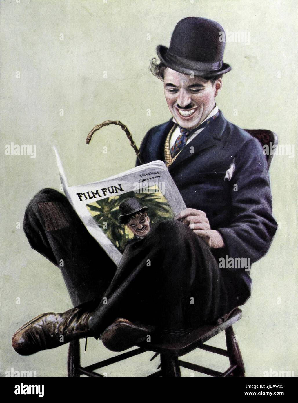 Ein Porträt von Charlie Chaplin aus dem Jahr 1915, aufgenommen als er 25 Jahre alt war. Er ist als Tramp gekleidet und liest mit sich selbst auf dem Cover die Zeitschrift Film Fun Stockfoto