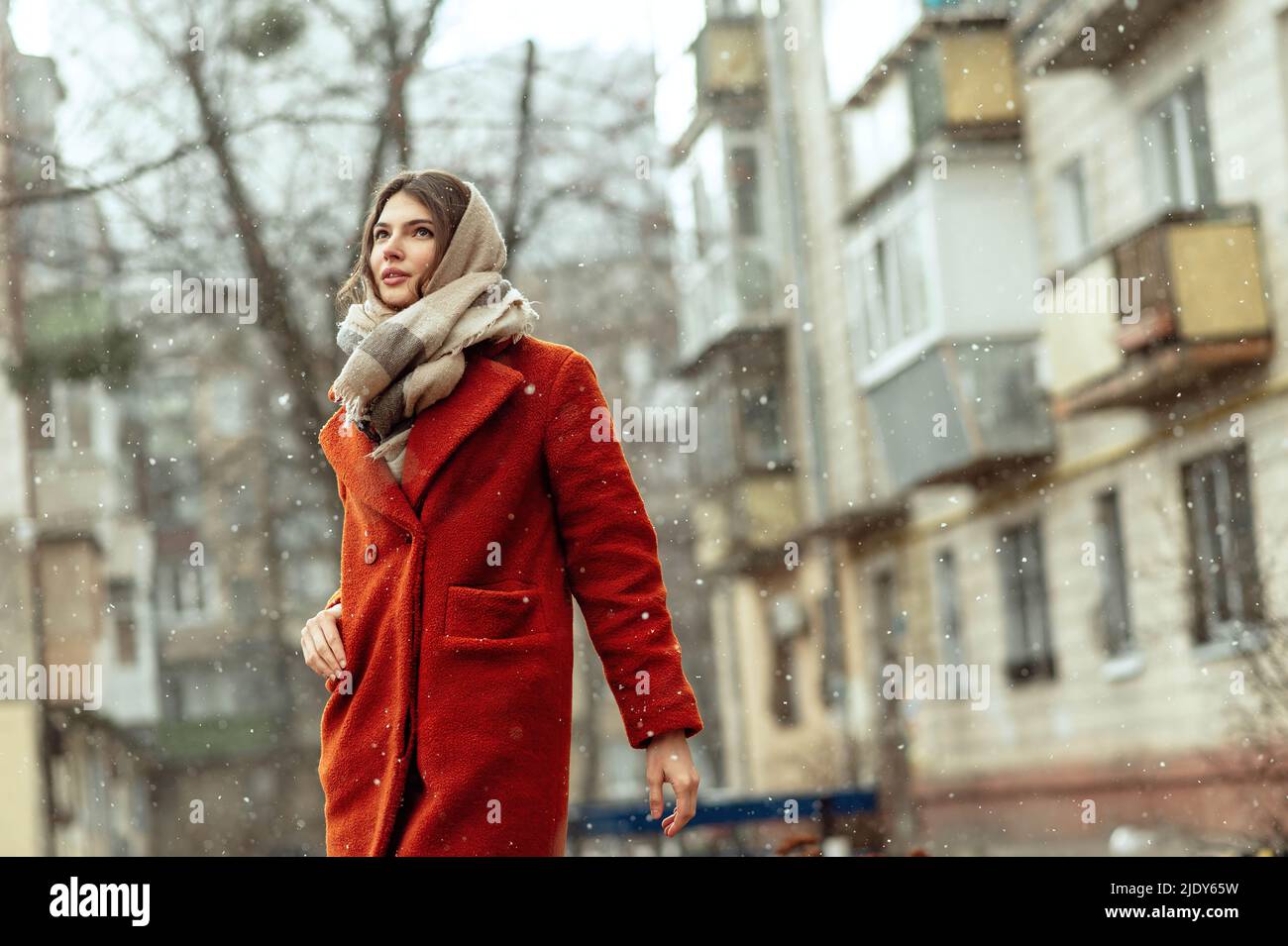 Schöne Brünette in einem roten Mantel auf einer Stadtstraße unter dem Schnee. Stockfoto