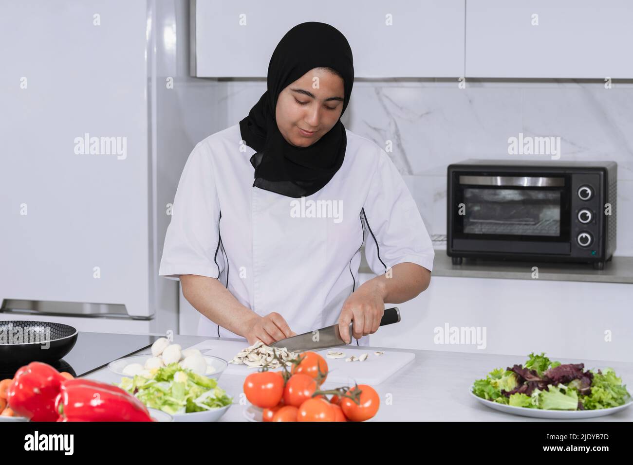 Maghrebi-Frau mit einem Hijab, der Pilze schneidet Stockfoto