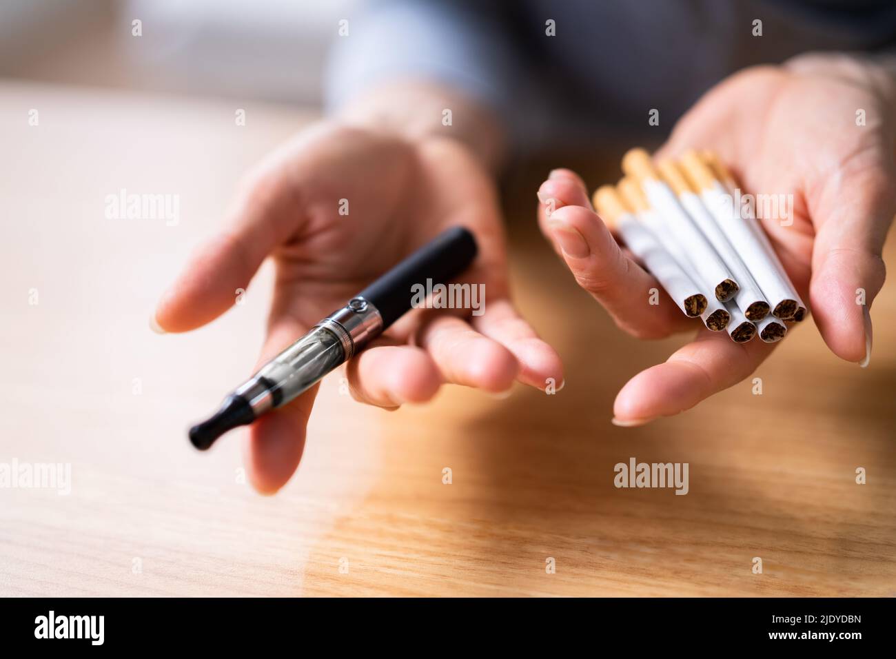 Woman's Hand hält Vape und Tobacco Zigaretten über dem Holzschreibtisch Stockfoto