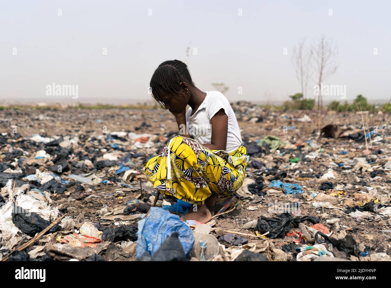 Müde kleines afrikanisches Mädchen, das verzweifelt im Müllhaufen nach Gegenständen sucht, die verwendet werden können; extreme Armut und Hoffnungslosigkeit der schwarzen c Stockfoto