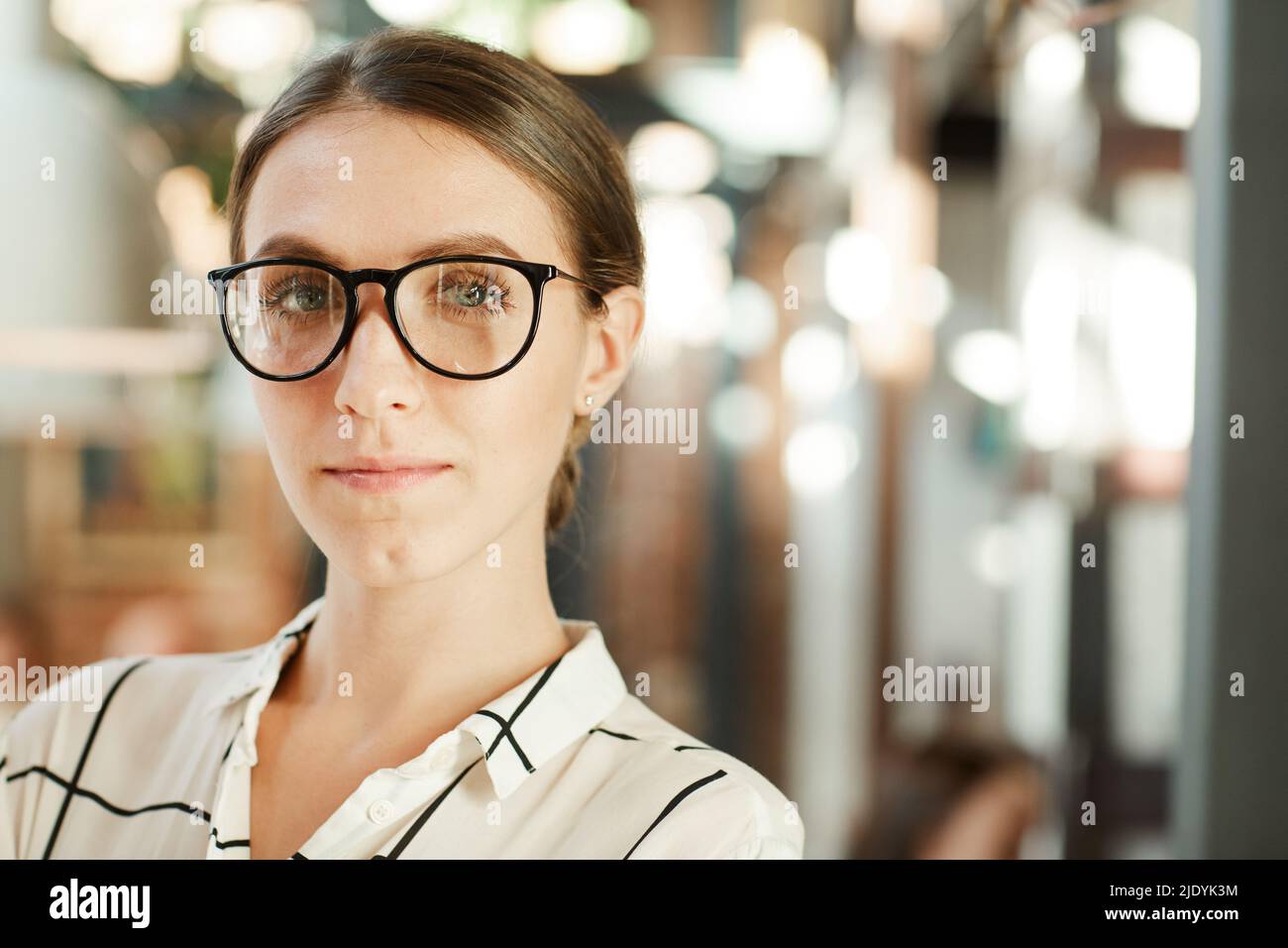 Portrait of content junge hübsche weibliche Spezialistin für stilvolle Brillen, die sich selbstbewusst gegen Lampen stehen Stockfoto