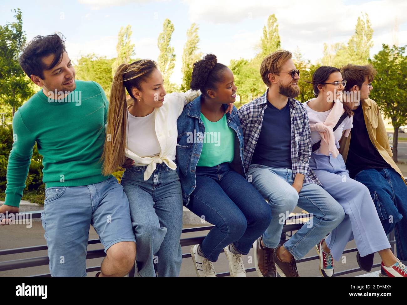 Sechs Hipster-Freunde sitzen während eines Sommerspaziergangs durch die Stadt auf einem Geländer einer Metallbrücke. Stockfoto