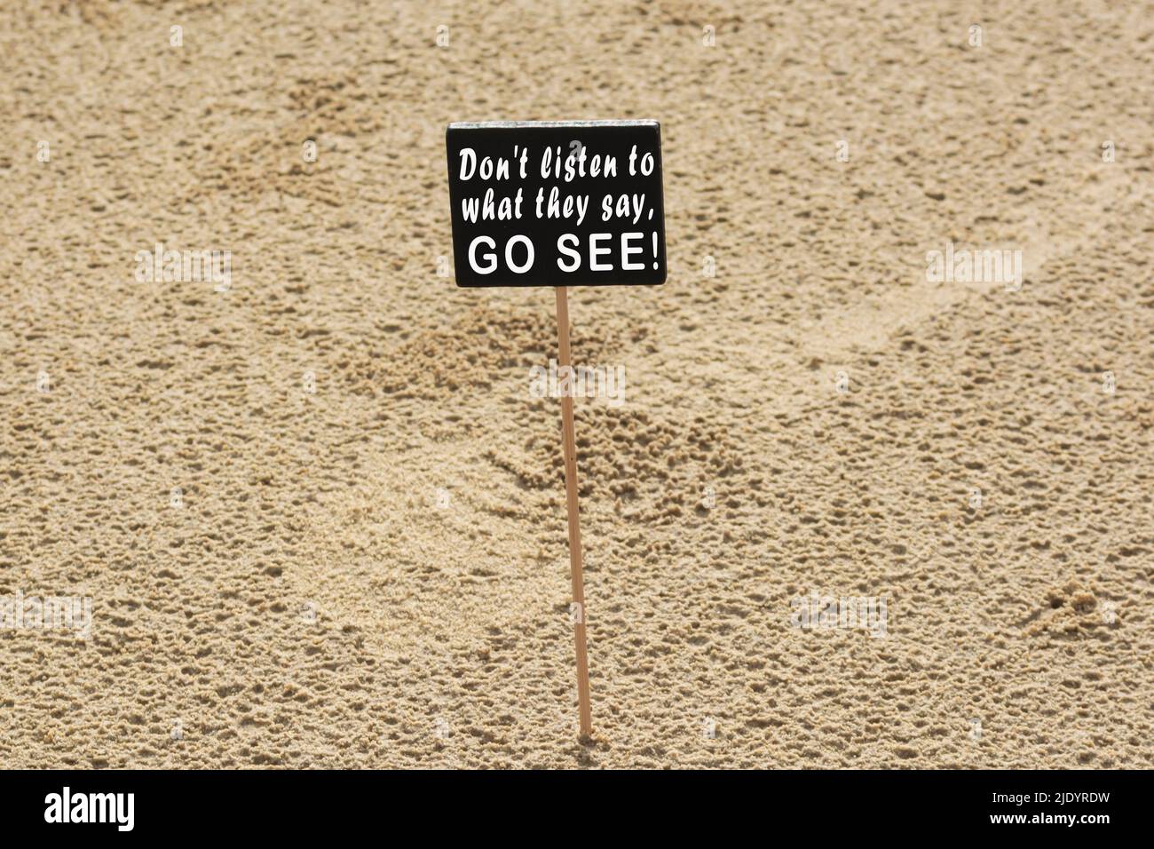 Motivierendes Zitat auf einer Tafel mit Hintergrund zum Sandstrand – hören Sie nicht zu, was sie sagen, sondern sehen Sie es sich an. Stockfoto