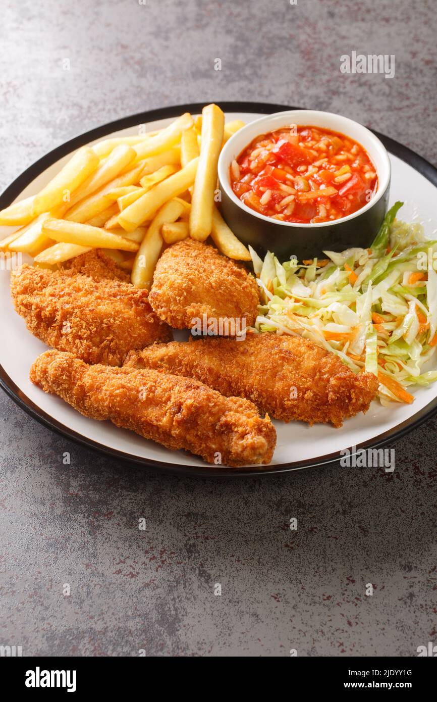 Paniertes gebratenes Huhn mit pommes Frites, Gemüsesalat und würziger Soße in Nahaufnahme auf einem Teller auf dem Tisch. Vertikal Stockfoto