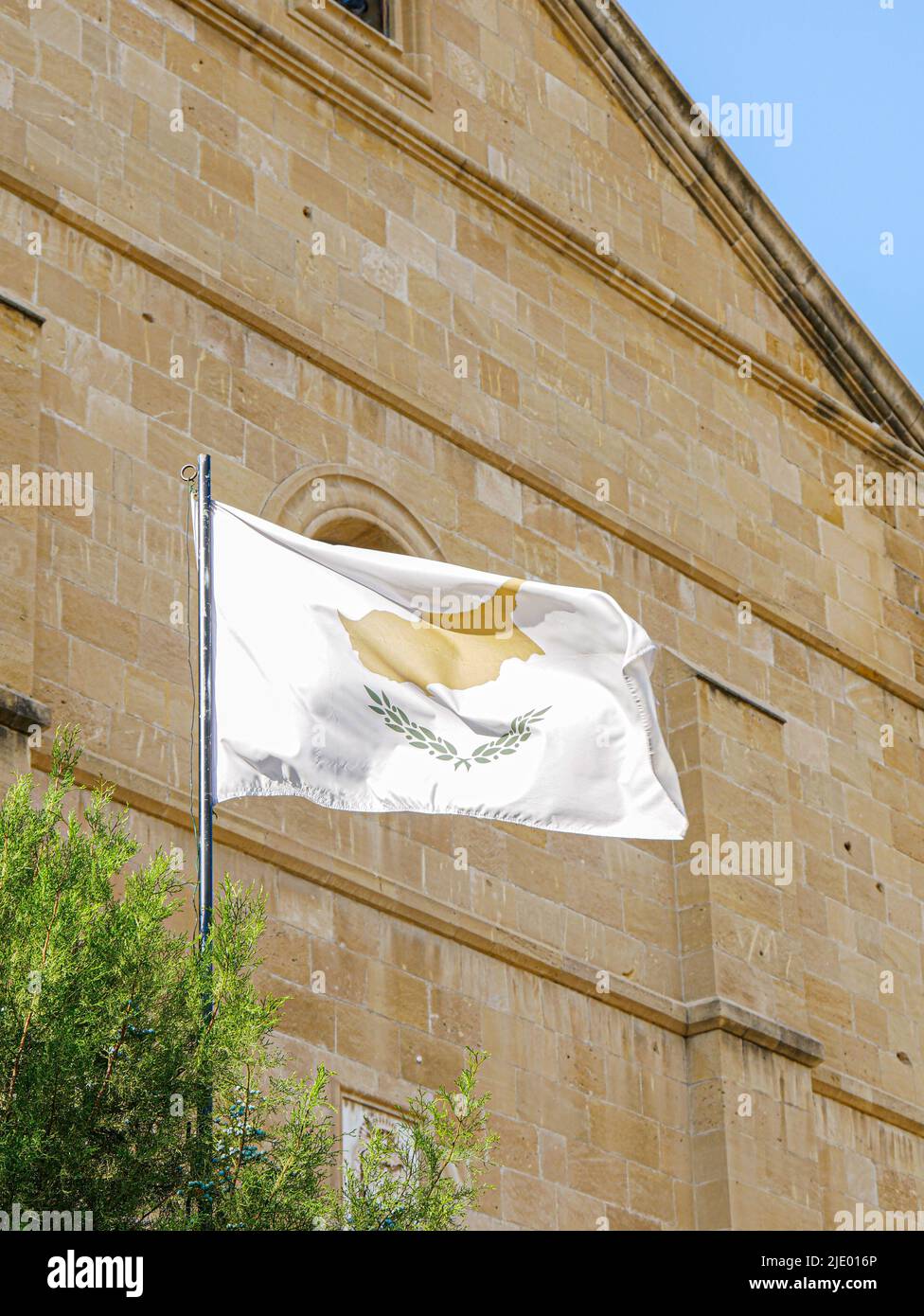 Vertikale Aufnahme einer zypriotischen Flagge, die in Nikosia, Zypern, mit einer Kirche im Hintergrund, geflogen ist Stockfoto