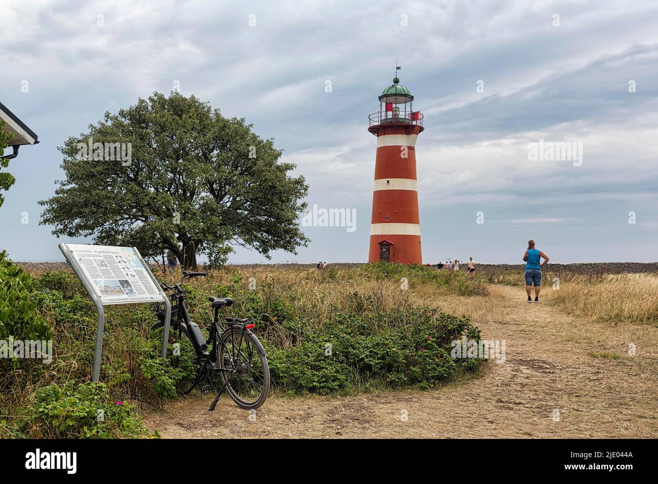 E-Bike steht an Informationstafel, rot-weißer Leuchtturm Naersholmen, Naerkholm Halbinsel, Gotland Insel, Schweden Stockfoto