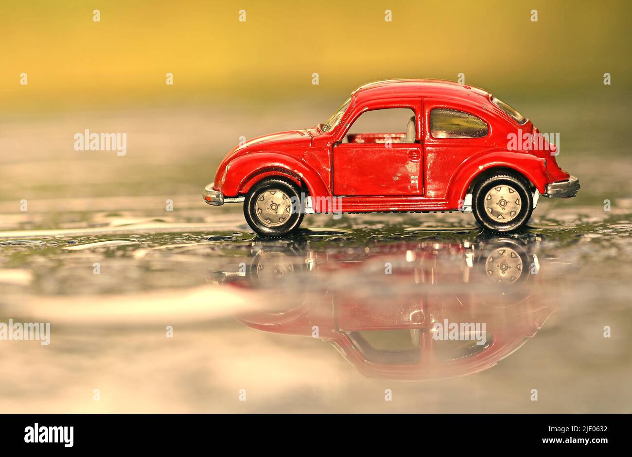 Rotes Spielzeugauto, VW Käfer mit Spiegelung auf regennasster Straße Stockfoto