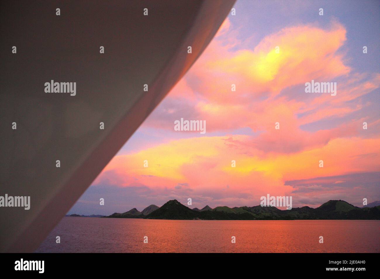 Farbenfrohe Himmel, Wolken über dem Meerwasser und hügelige Landschaft um die Sonnenuntergangszeit sind von einem Boot im Komodo Nationalpark in Komodo, West Manggarai, Ost-Nusa Tenggara, Indonesien, zu sehen. Stockfoto