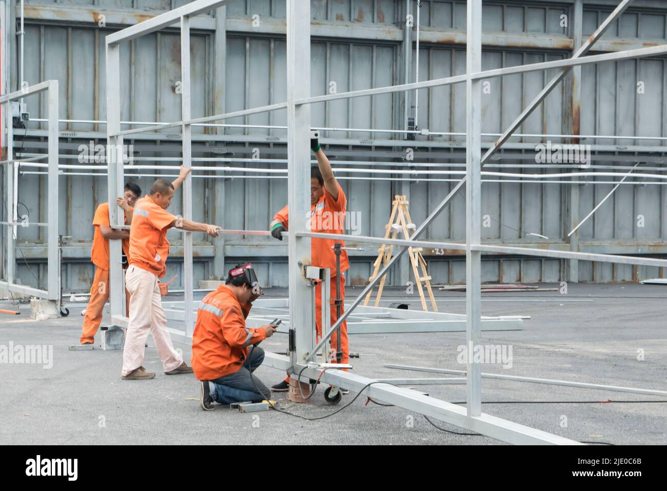 Eine Gruppe chinesischer Bauarbeiter arbeiten zusammen, um eine Stahlkonstruktion eines Hangars durch Schweißen von Metallen zu montieren. Stockfoto