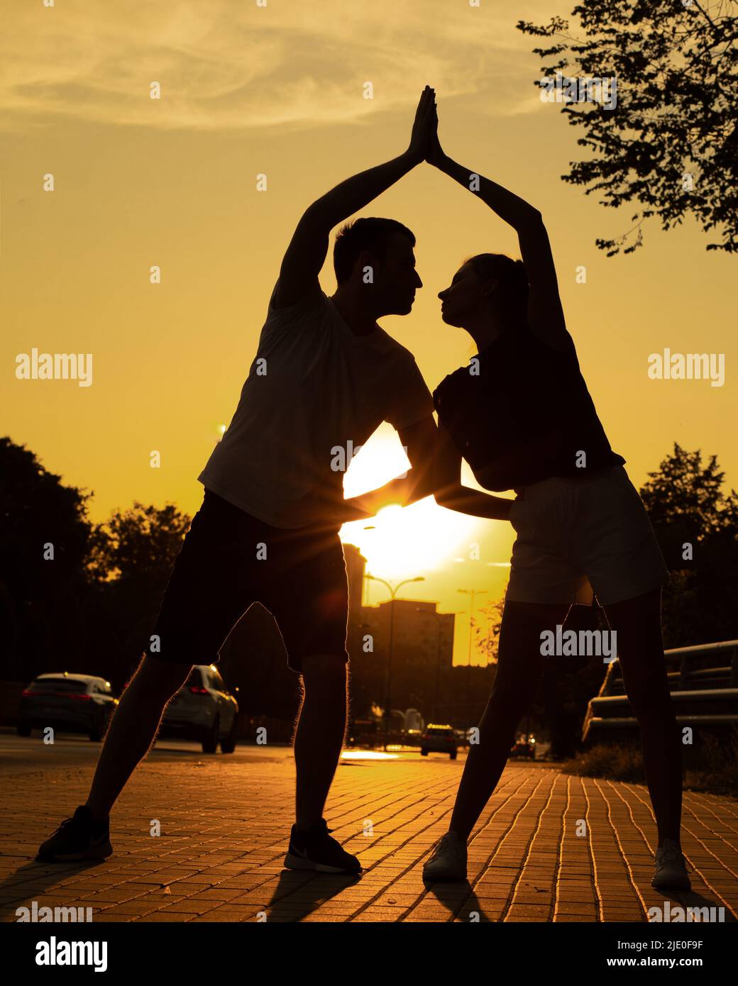 Junges Paar trainieren auf Straße in der Nähe von Straße in der Stadt von unten, Sonnenuntergang Hintergrund. Abgedunkelte Silhouetten von trainingsorientierten Männern und Frauen, die auf jeden Blick schauen Stockfoto