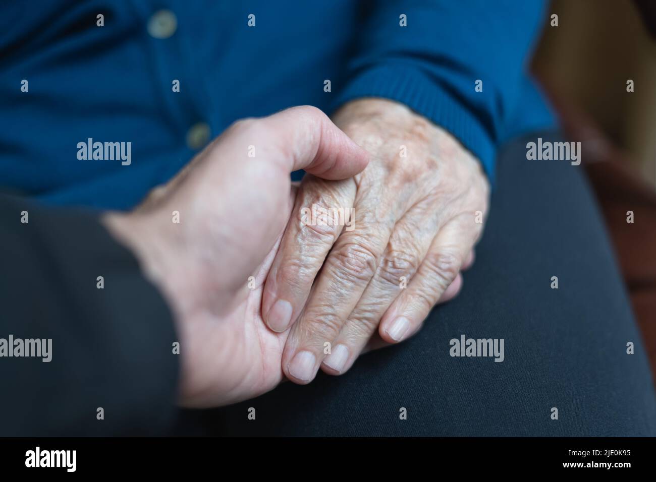 Die Hand des jungen Mannes, der die Hand der älteren Frau in fürsorglicher und helfender Haltung hält. Stockfoto