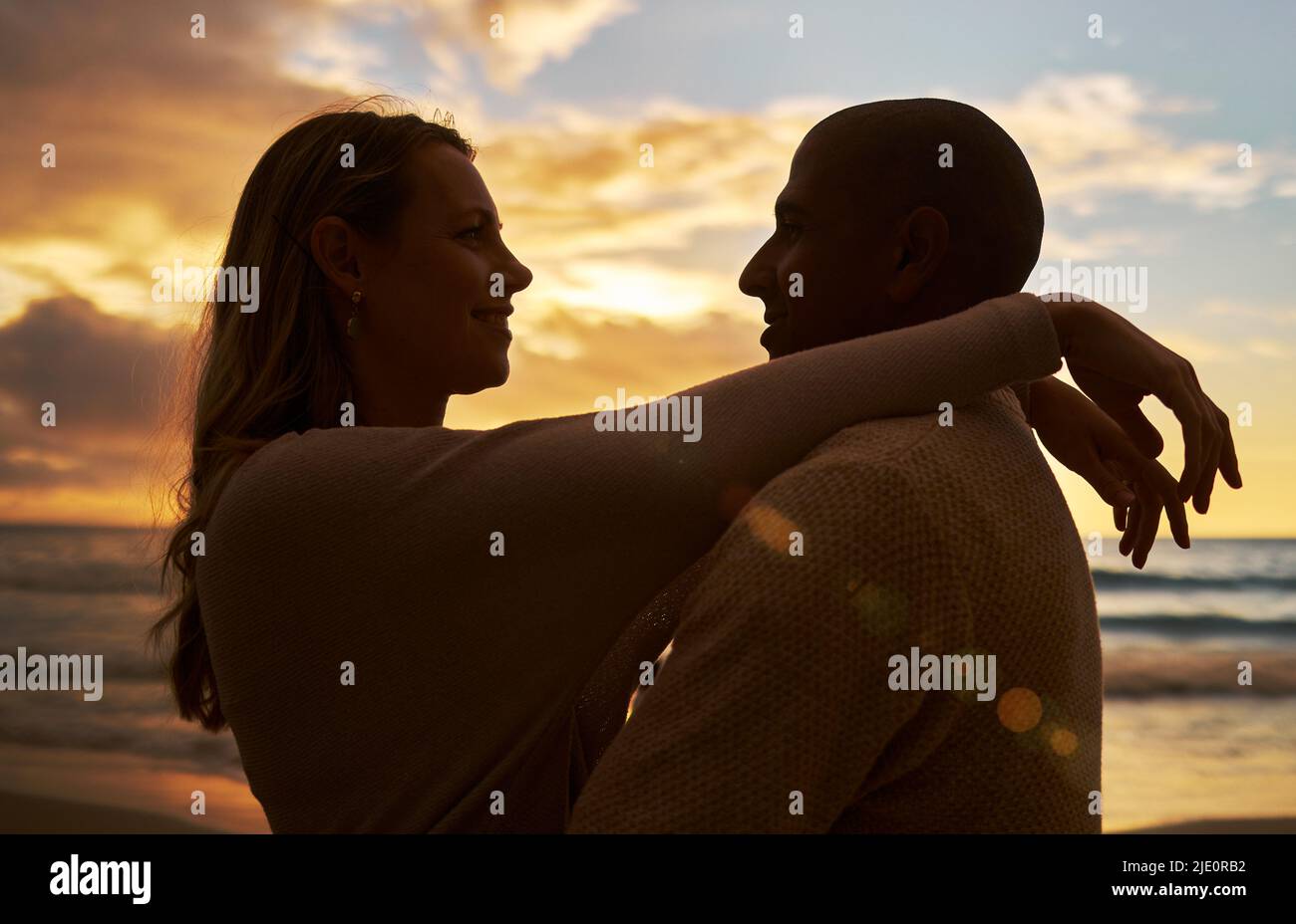 Liebevolles junges, liebevolles interracial Paar in Silhouette, das sich gegenübersteht, während es Zeit zusammen am Strand bei Sonnenuntergang verbringt. Liebe zum Teilen Stockfoto
