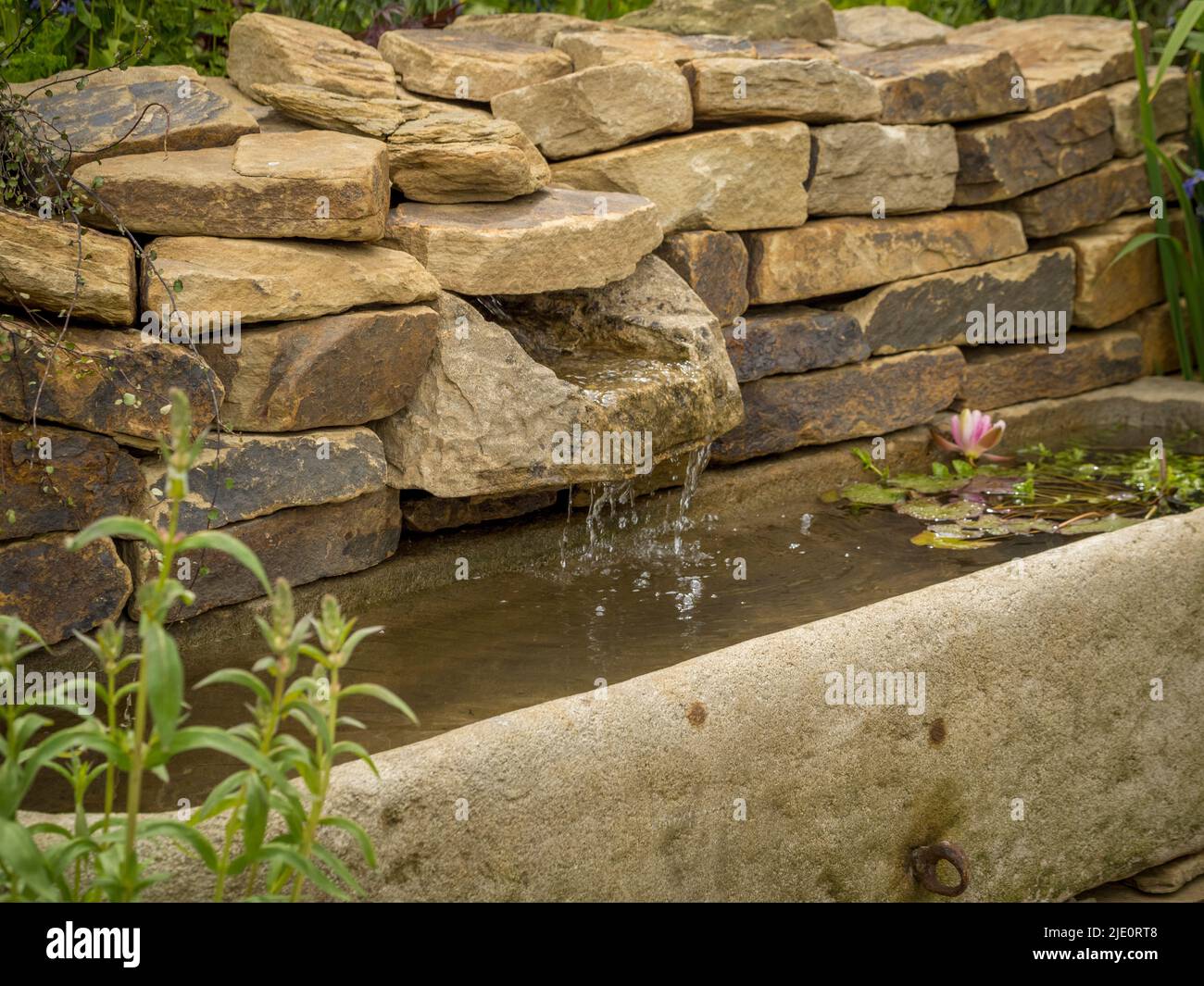 Das Wasser in einer trockenen Wand fließt in einen alten Wassertrog in einem britischen Garten. Stockfoto