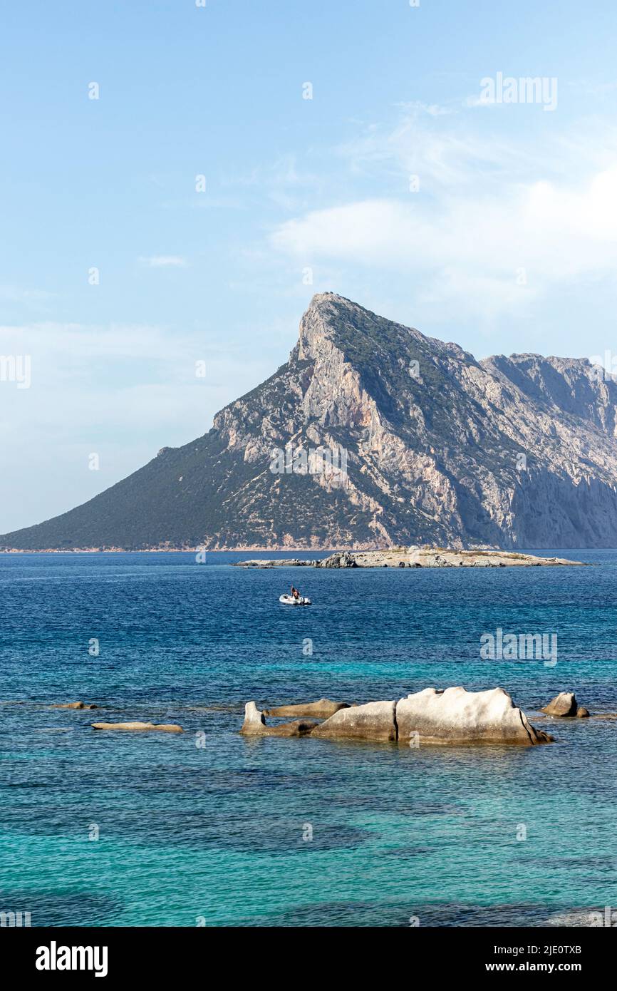 Vertikale Ansicht der sardischen Berglandschaft im Hintergrund, türkisfarbenes Wasser und Boot in der Mitte Stockfoto