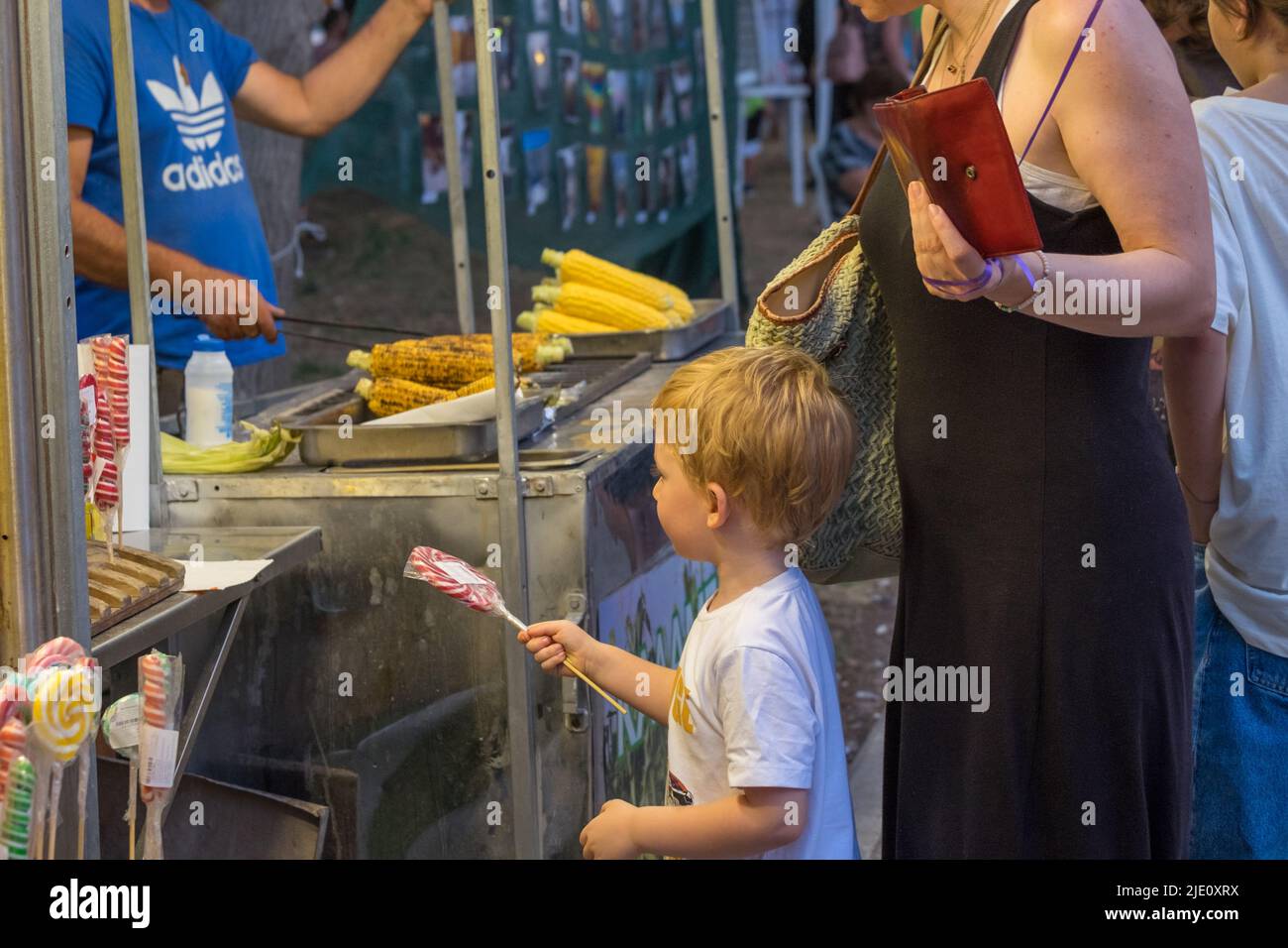 Mutter kauft einen Lutscher für ihren kleinen Sohn von einem Maisstandplatz während eines Festivals oder einer Veranstaltung Stockfoto