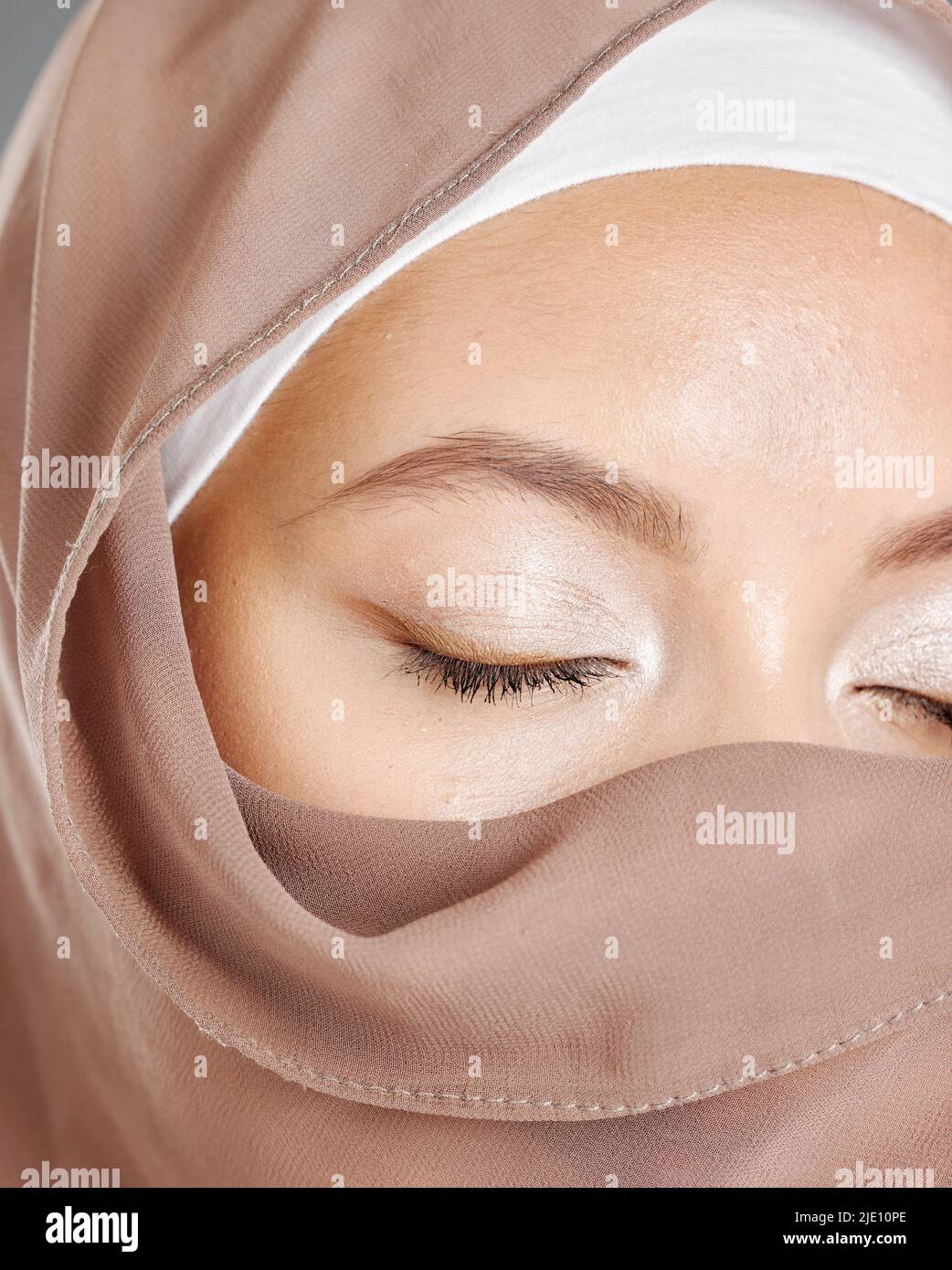 Bescheidene arabische Frau, die Make-up trägt und das Gesicht mit einem braunen traditionellen Hijab bedeckt ist. Nahaufnahme einer schönen jungen muslimischen Frau mit strahlender Haut und Stockfoto