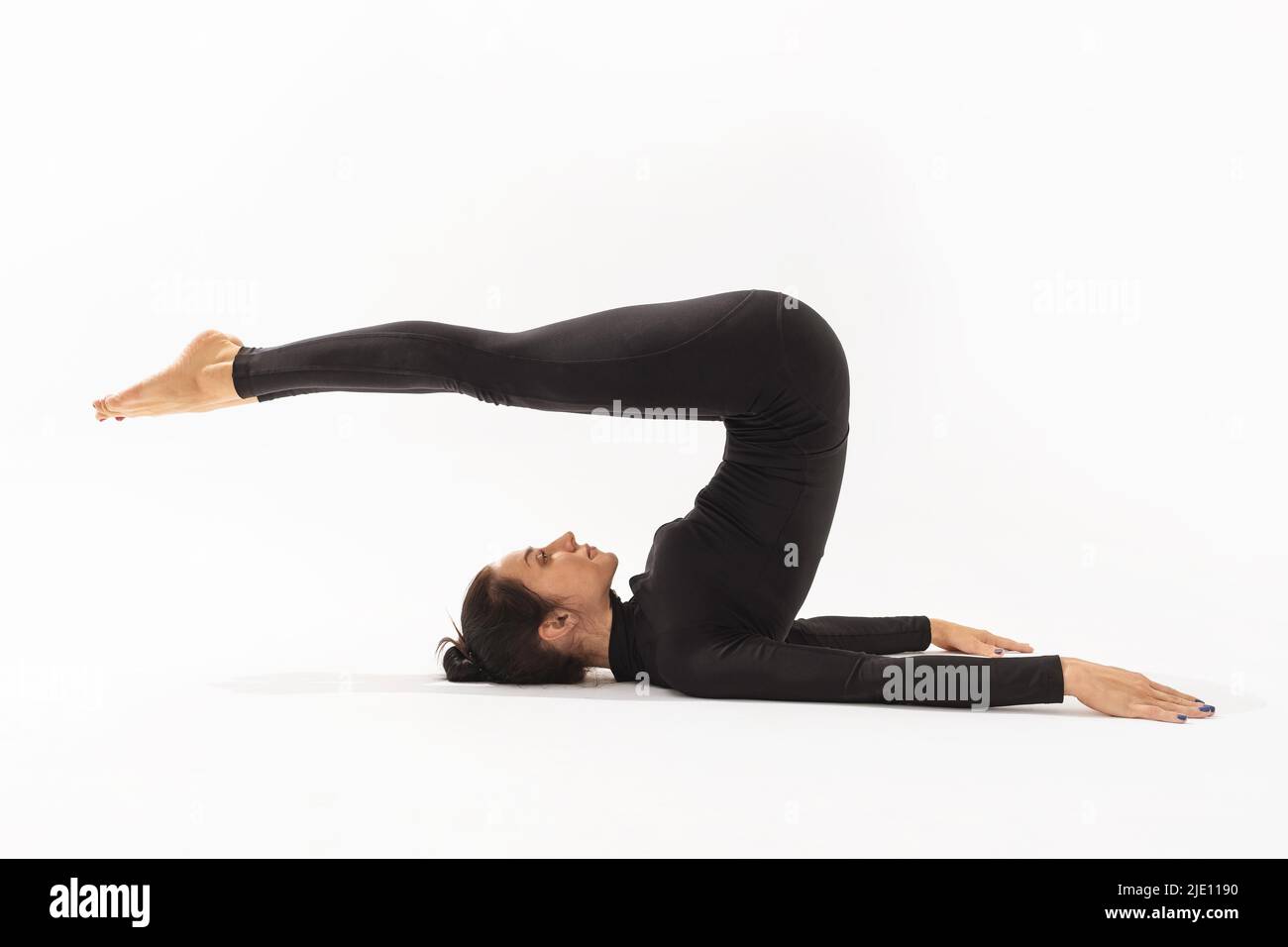 Frau in schwarzer Sportkleidung, die Yoga praktiziert, Halasana-Übung macht, Pose auf weißem Hintergrund pflügen Stockfoto