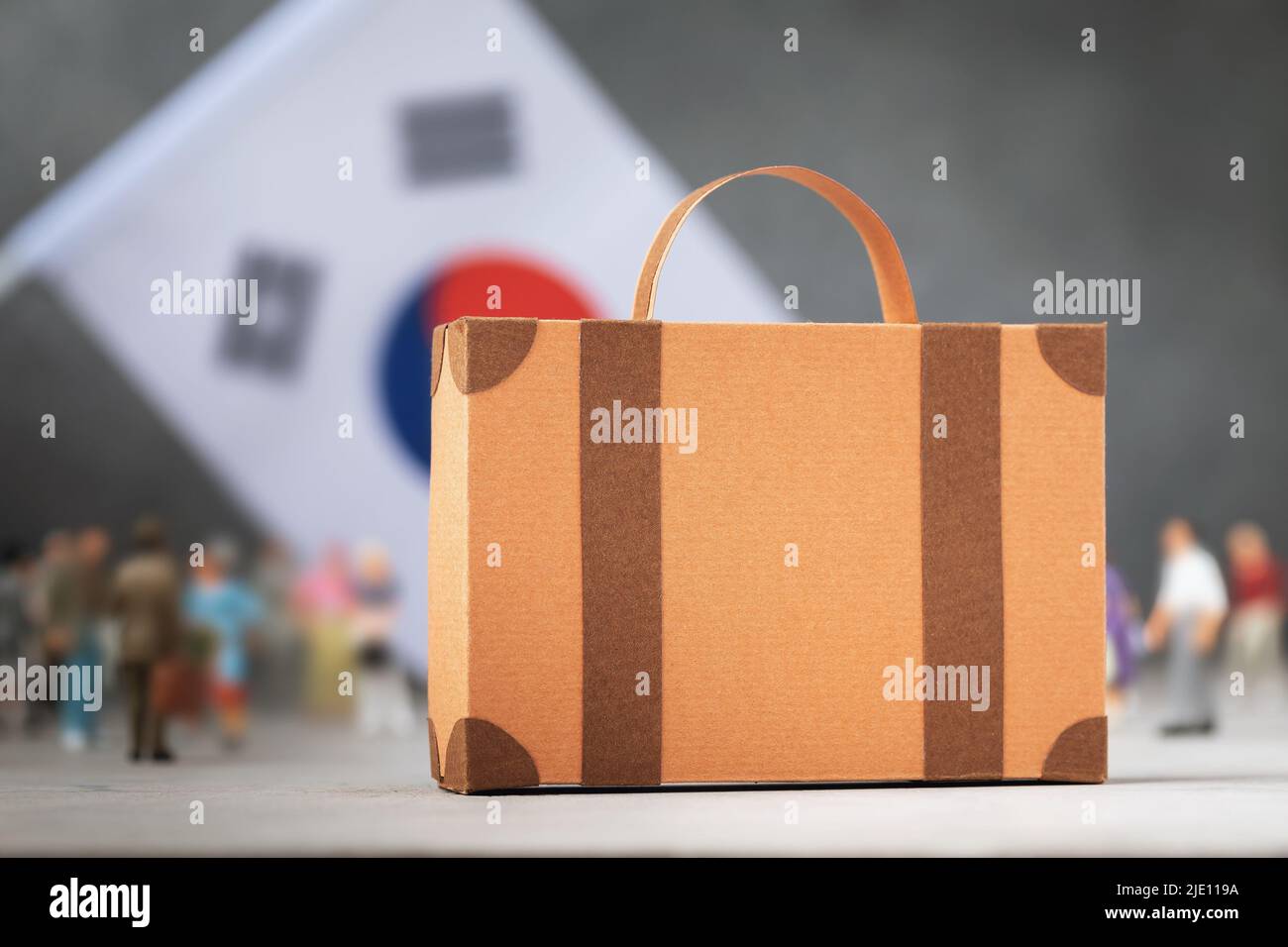 Pappkoffer, Plastikspielzeug Menschen und eine Flagge auf abstraktem Hintergrund, ein Konzept zum Thema Umzug oder Migration nach Südkorea Stockfoto