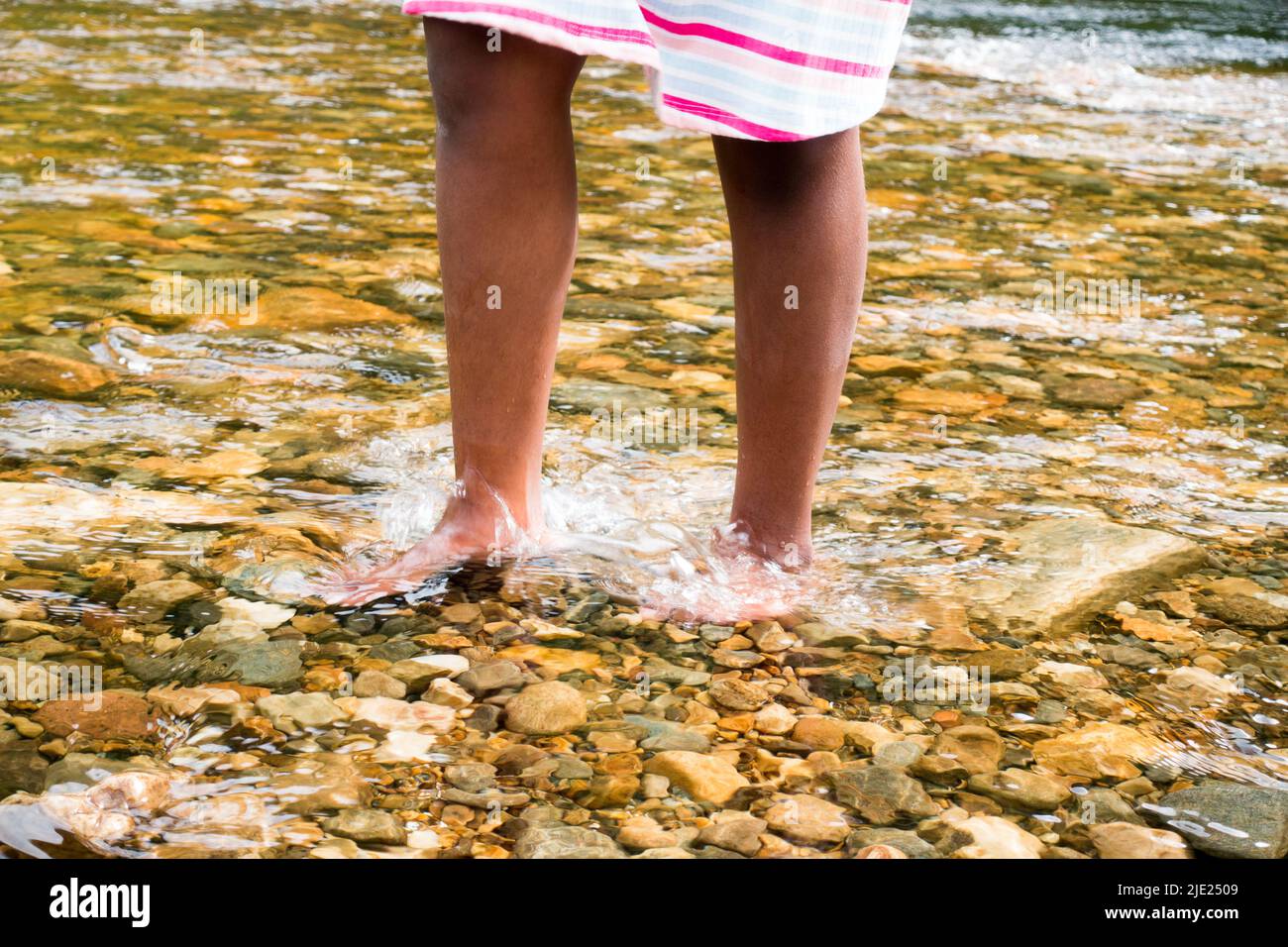 Junges Mädchen im Alter von 8 Jahren, das im kalten Wasserbach mit Kieselsteinboden läuft Stockfoto
