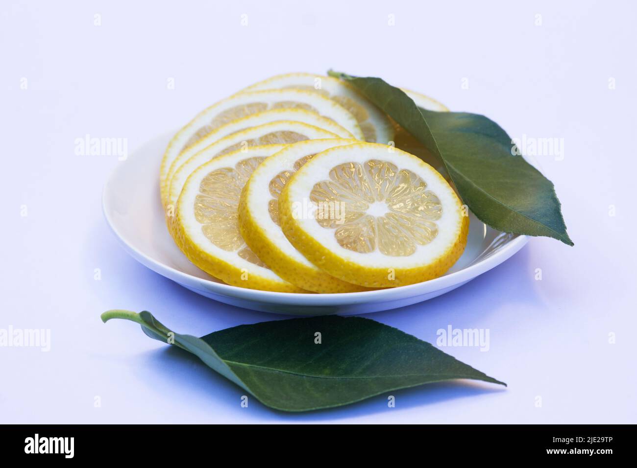 Geschnittene Zitronen und grüne Blätter auf einem weißen Teller isoliert auf weißem Hintergrund Stockfoto