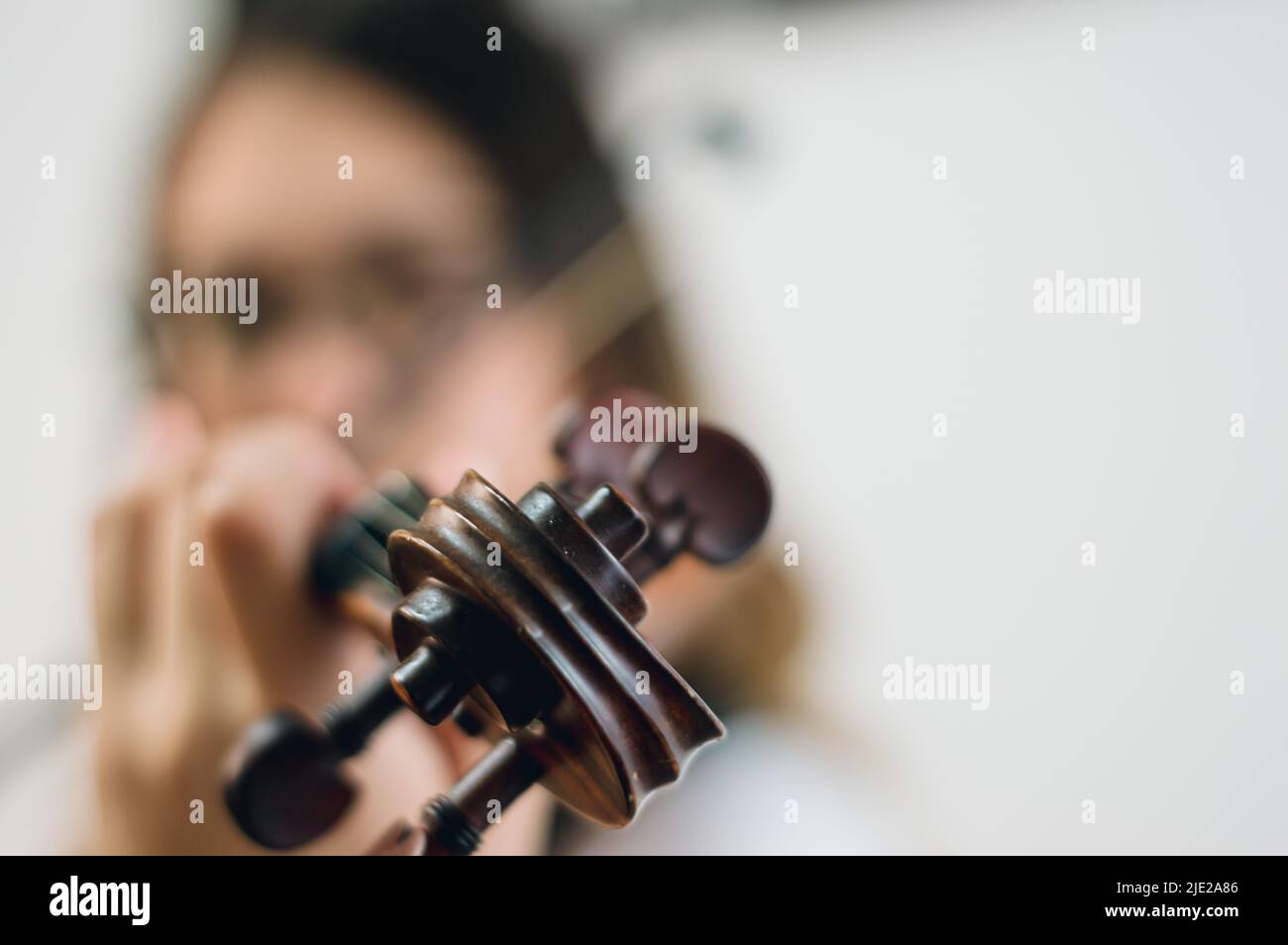 Nahaufnahme von Rollen und Stöpseln der Geige mit einer unscharfen Frau, die im Hintergrund spielt und Raum nach rechts kopiert, Musikkonzept. Stockfoto