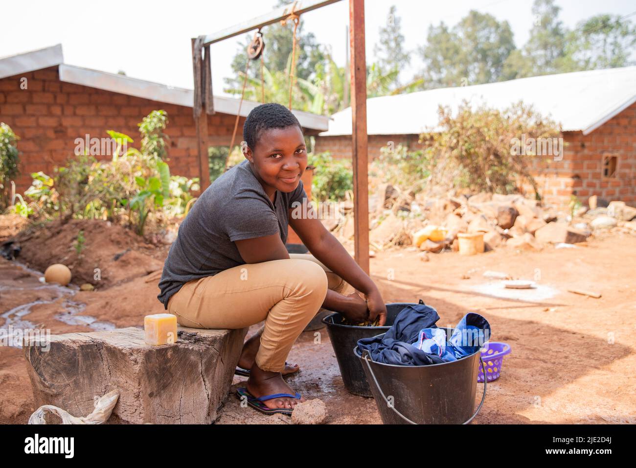 Junge afrikanische Mädchen wäscht Kleidung draußen mit Waschseife und einem Eimer Stockfoto