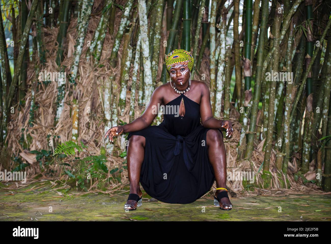 Afrikanische Stammesfrau sitzt im Dschungel mit Gesichtsbemalung und Kopfschmuck Stockfoto