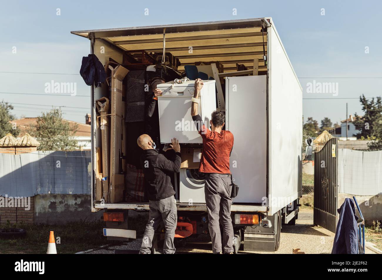 3 Kollegen eines Umzugsunternehmens laden einen Geschirrspüler auf den LKW Stockfoto