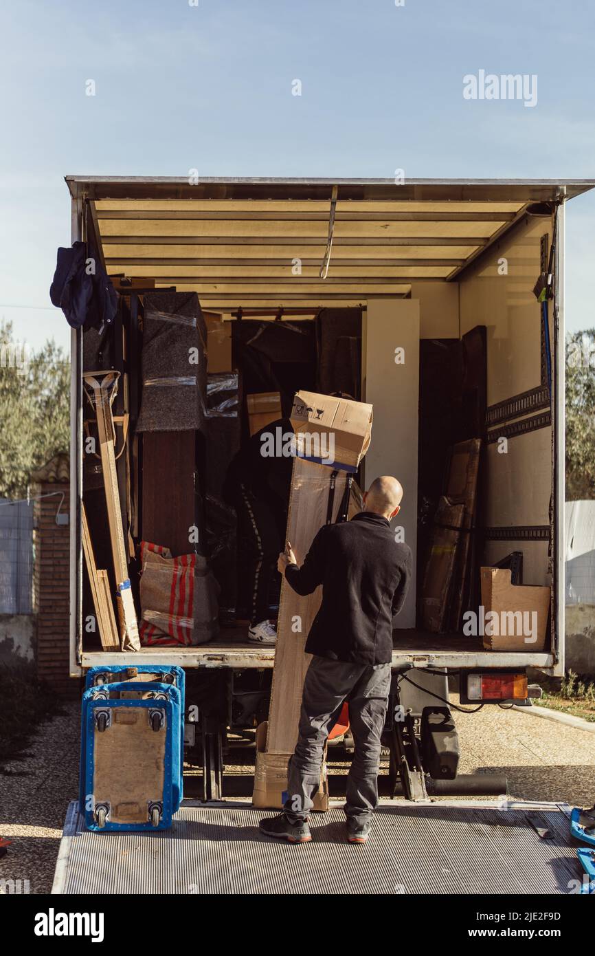 Glatzkopf hält das Paket, während ein Kollege versucht, es auf einen fahrenden Lkw zu heben Stockfoto