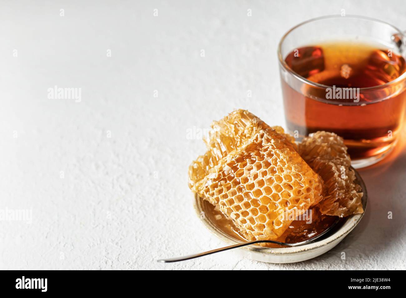 Honig in Honigwabe in einer Untertasse mit Löffel und einer Tasse Tee auf weißem Hintergrund. Textort. Horisontale Ausrichtung Stockfoto